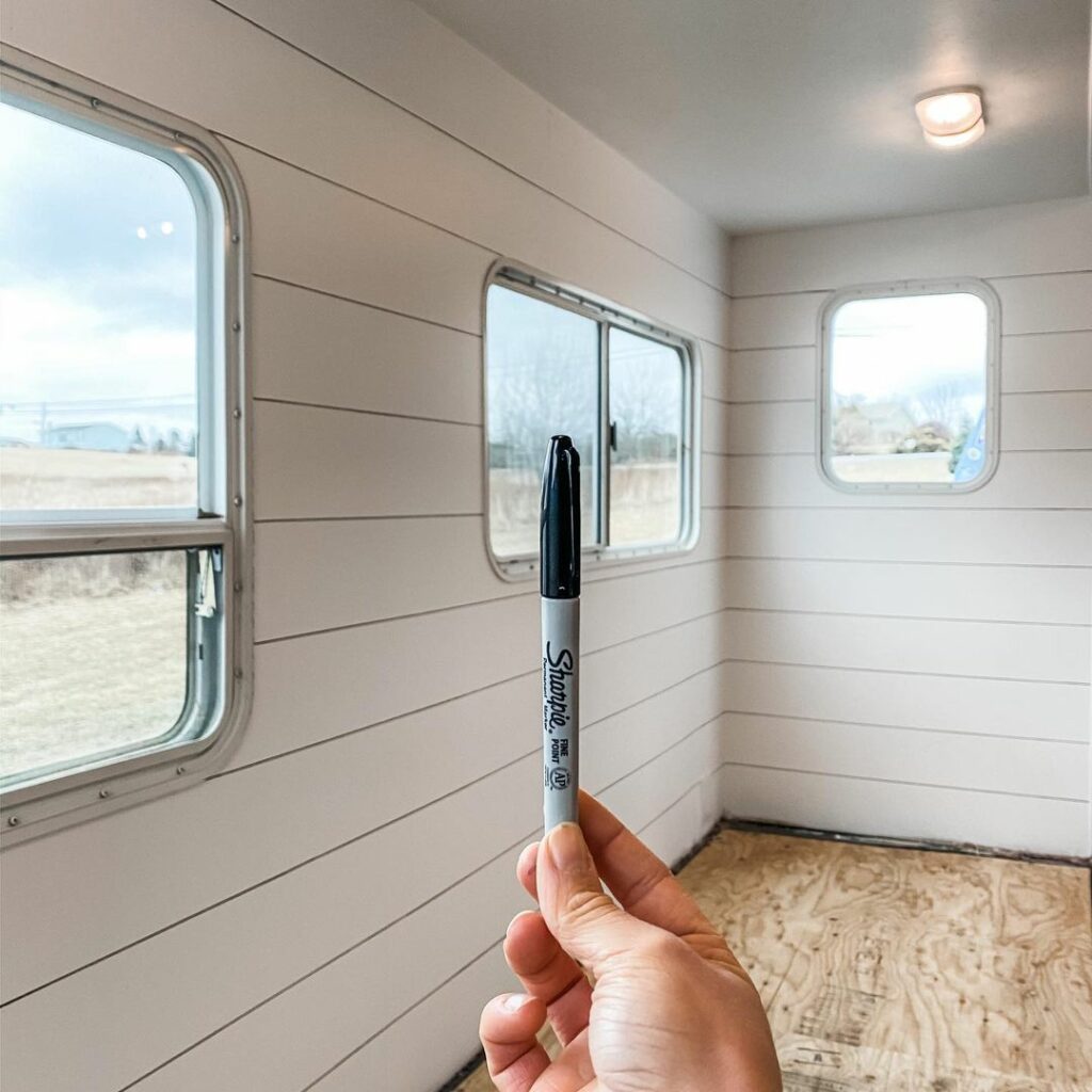 Hand holding a Sharpie permanent marker vertically in front of a faux Sharpie shiplap wall inside an RV